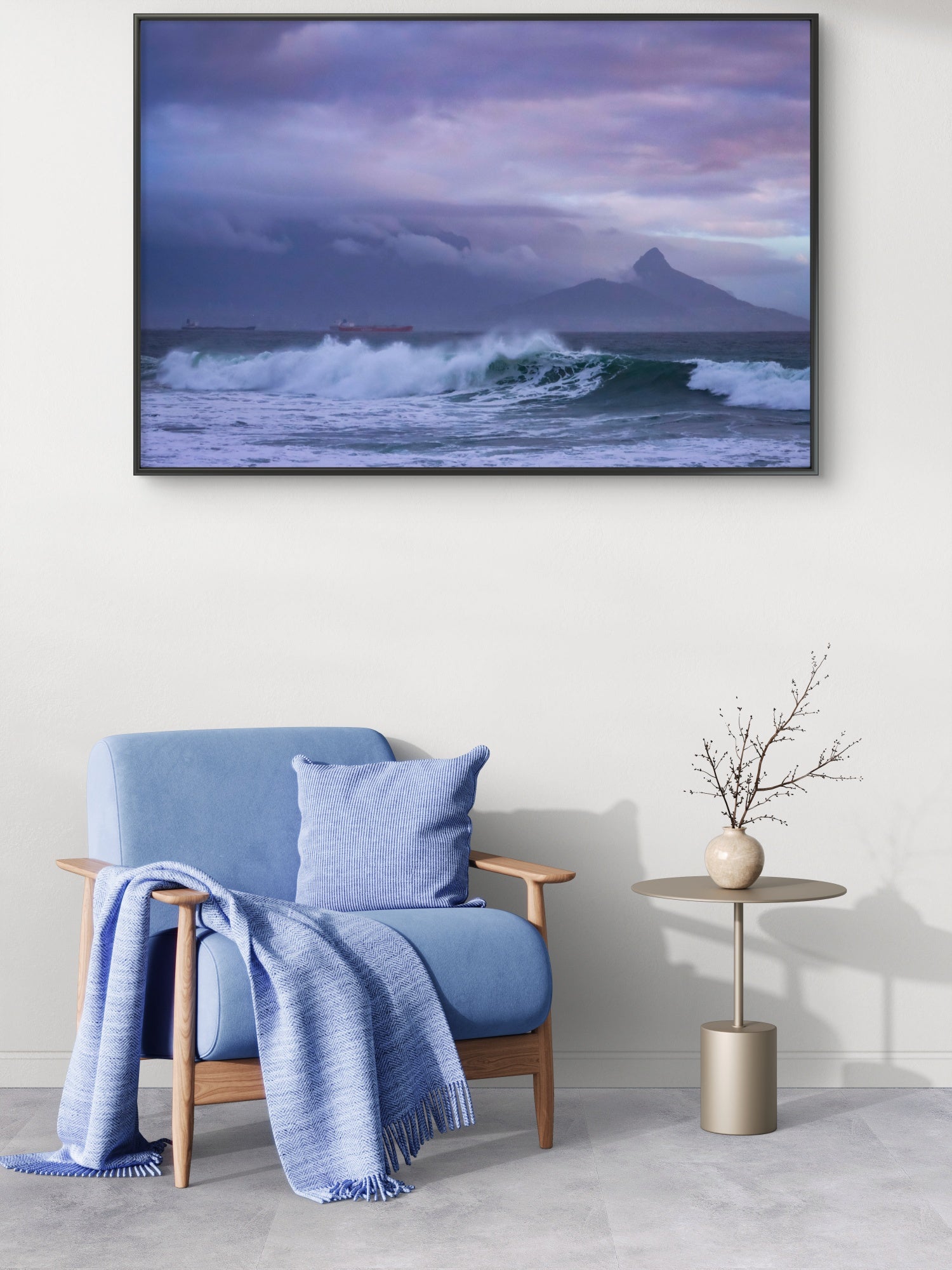 Blue armchair with a blanket and pillow in a room with a large framed picture of a mountain and ocean.