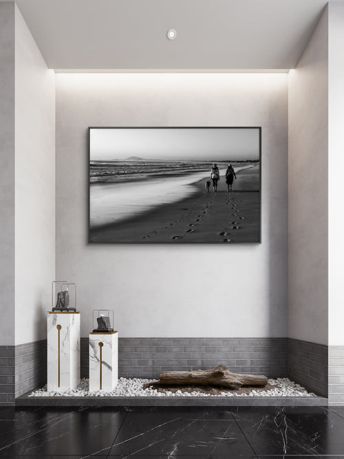 Framed black and white artwork of a beach scene with people and a dog, displayed on a wall in a modern interior setting.