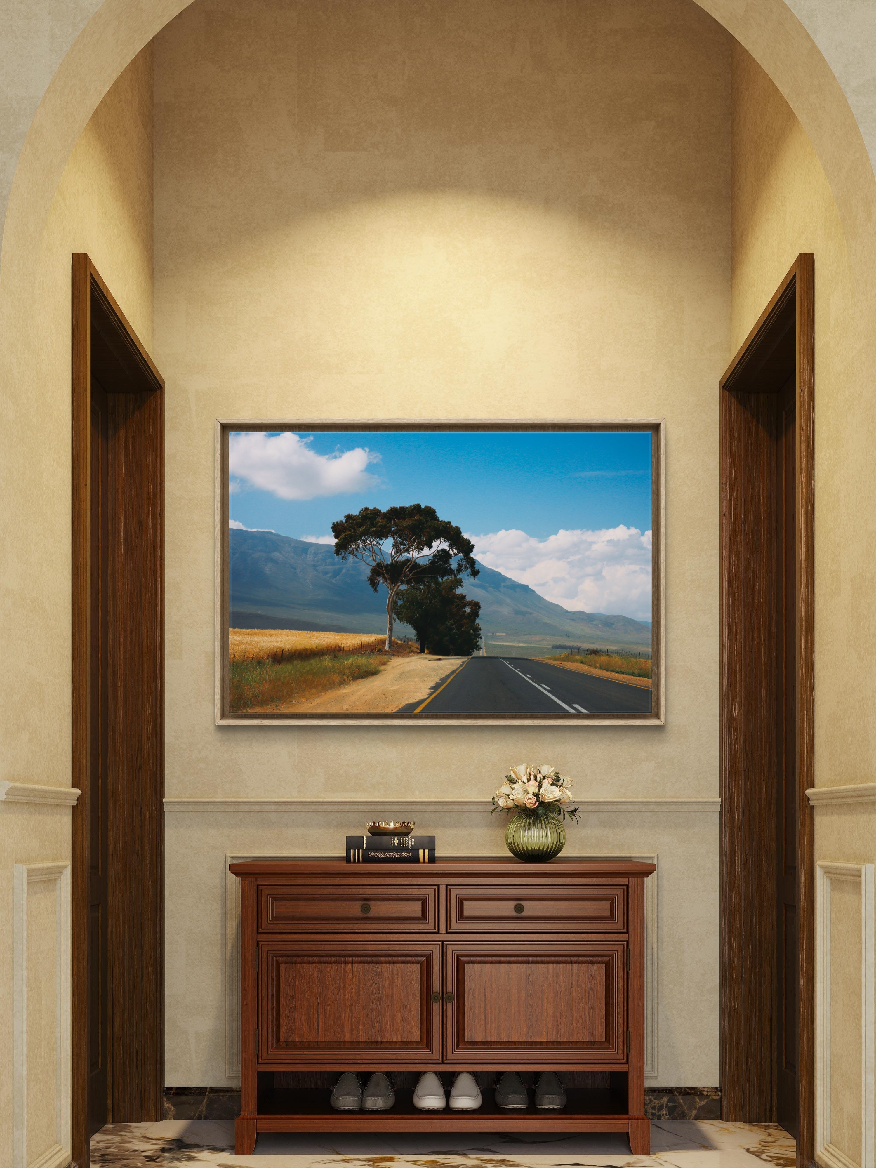 Framed landscape painting above a wooden cabinet in a room with arches.