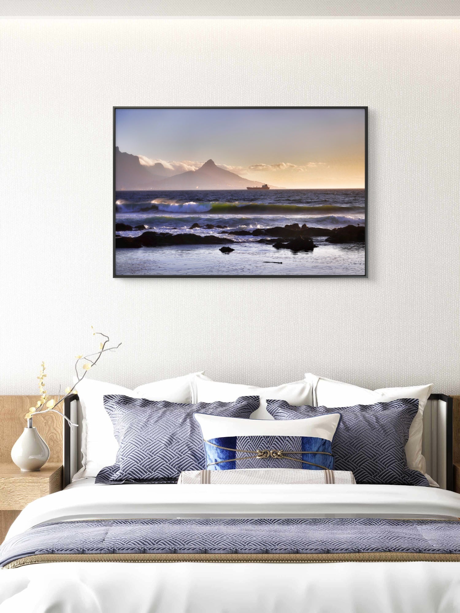 Framed artwork of a coastal scene above a bed with white bedding and blue pillows.