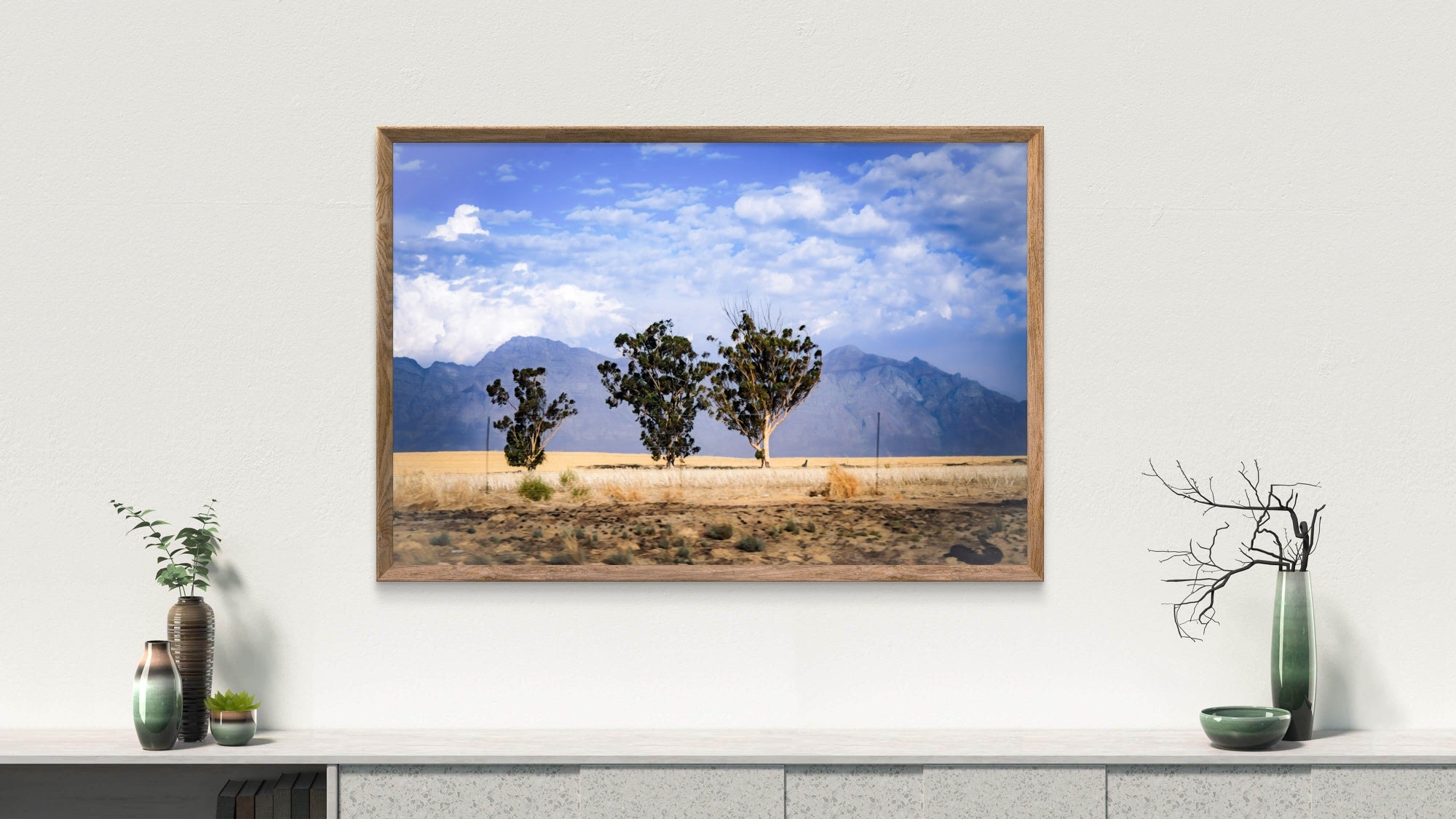 Framed landscape print of trees and mountains on a wall above a shelf with decorative items.