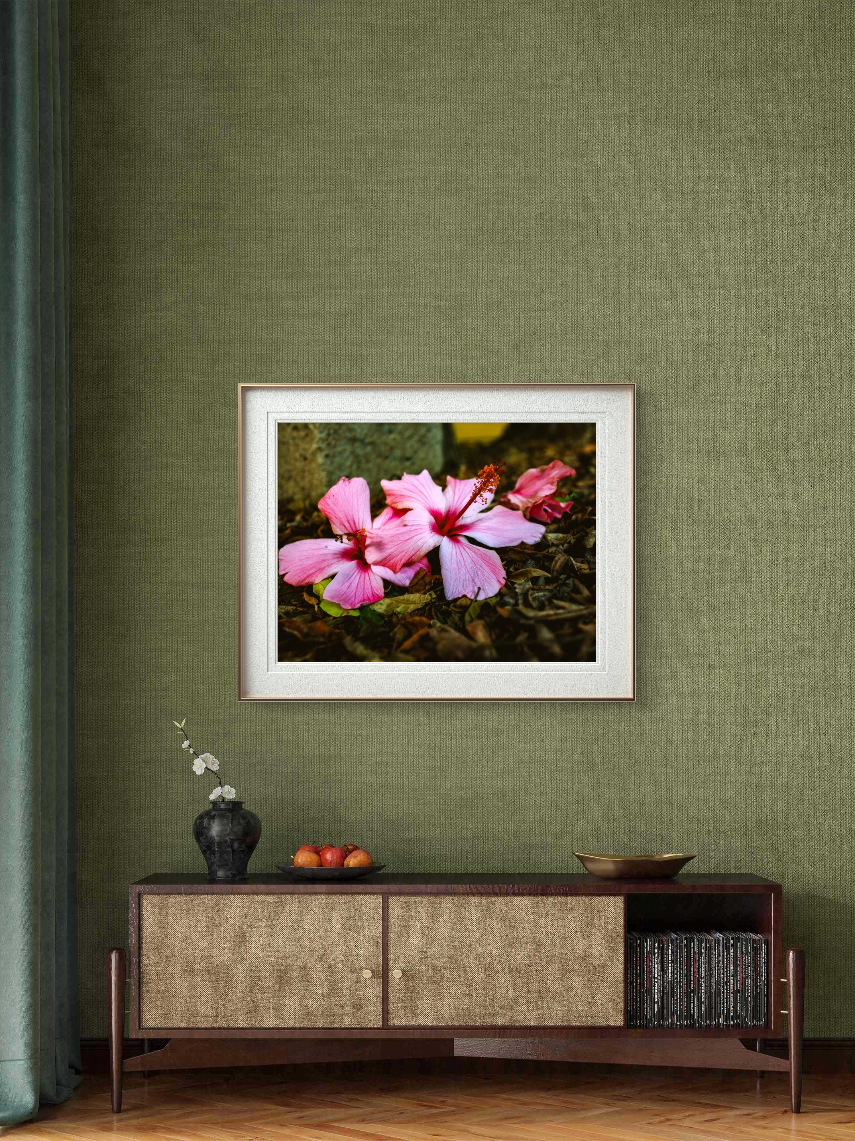 Framed photograph of pink flowers on a green wall above a wooden cabinet.