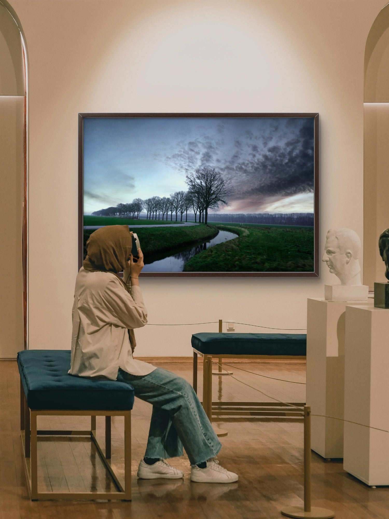 Woman sitting on a bench in a gallery, looking at a large screen displaying a scenic landscape.