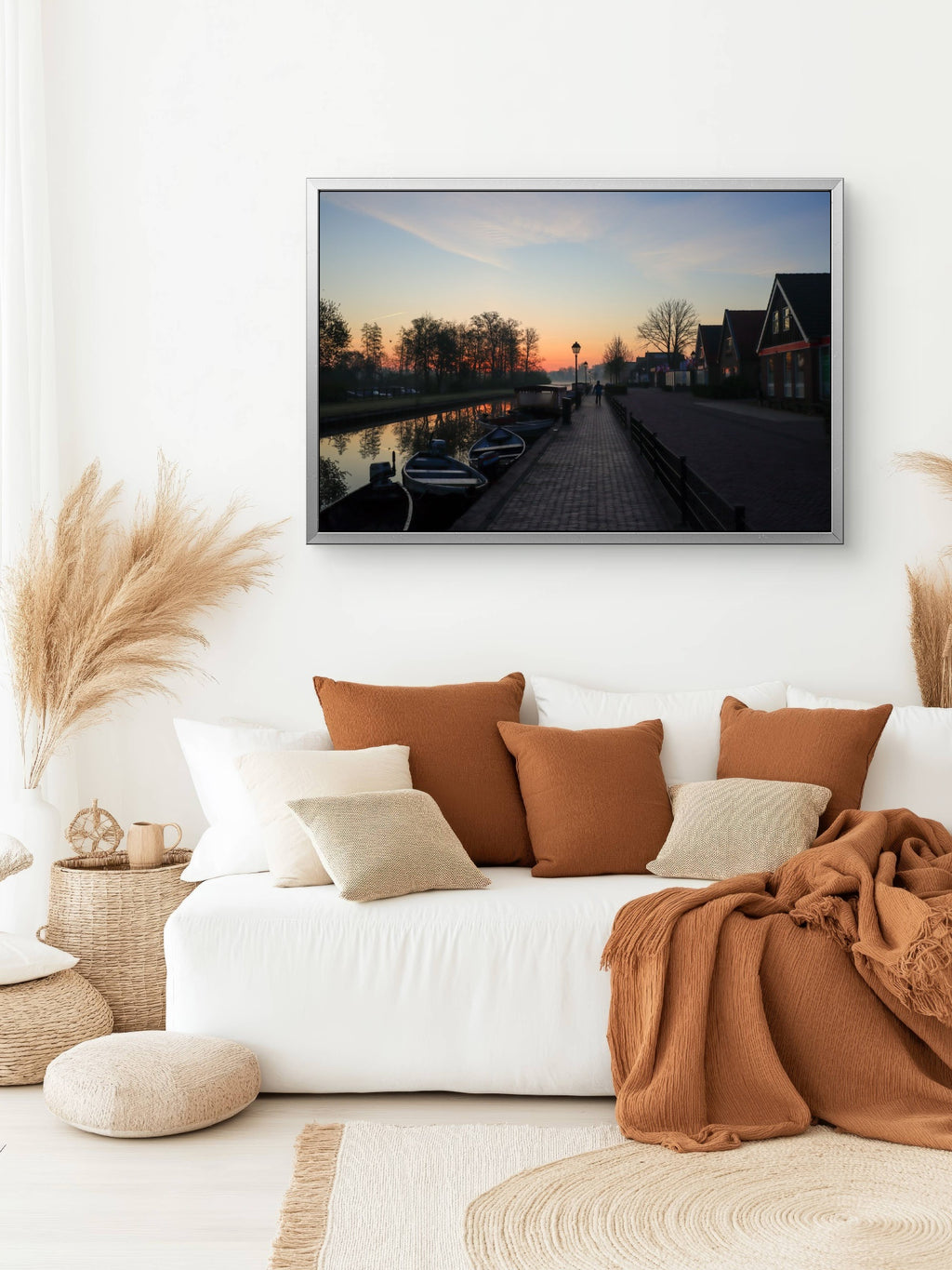 Cozy living room with a white sofa, brown cushions, and a framed picture of a sunset over a canal.