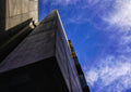 Worm's-eye view of a brutalist concrete building corner against vivid cobalt blue sky, dramatic shadow and geometric lines.