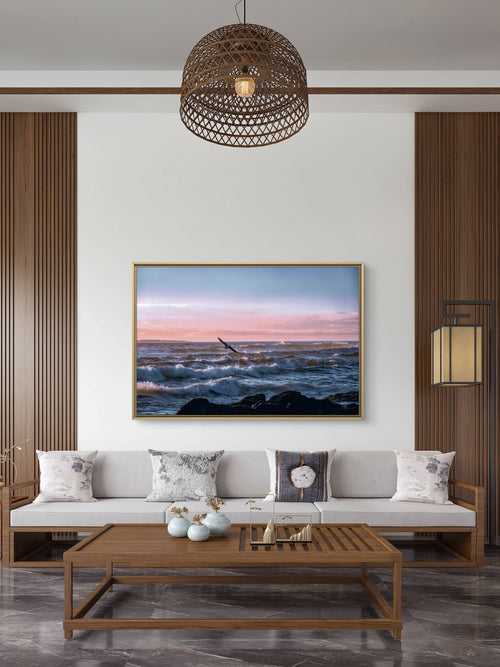 Modern living room with a sofa, coffee table, and wall art depicting a sunset over water.
