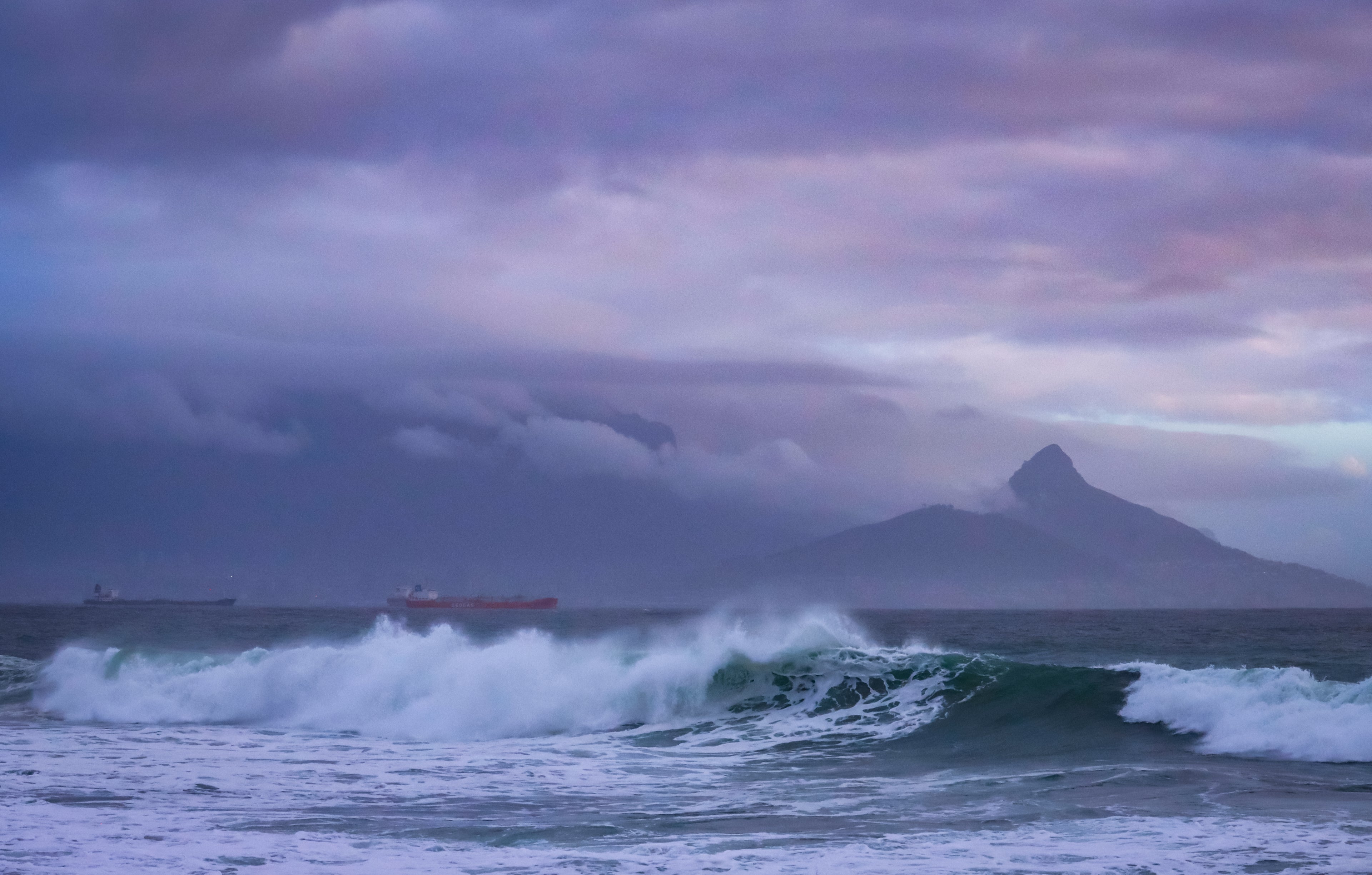 Fine art photograph of dramatic storm swells breaking on the Cape Town coast with Lion's Head silhouetted under a purple and mauve storm sky. Photography Wall Art Print.