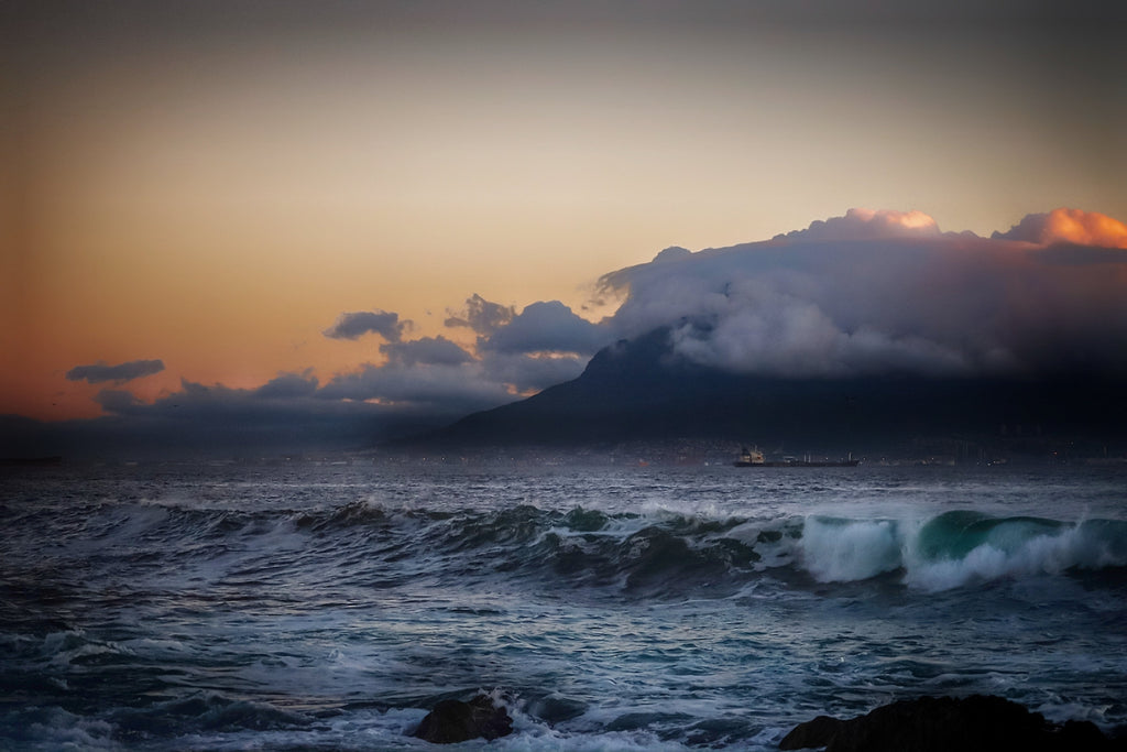 Fine art photograph of Table Mountain shrouded in storm cloud at dusk with dark Atlantic swells and amber sky over Table Bay, Cape Town South Africa seascape wall art print, ApertureAndArt.
