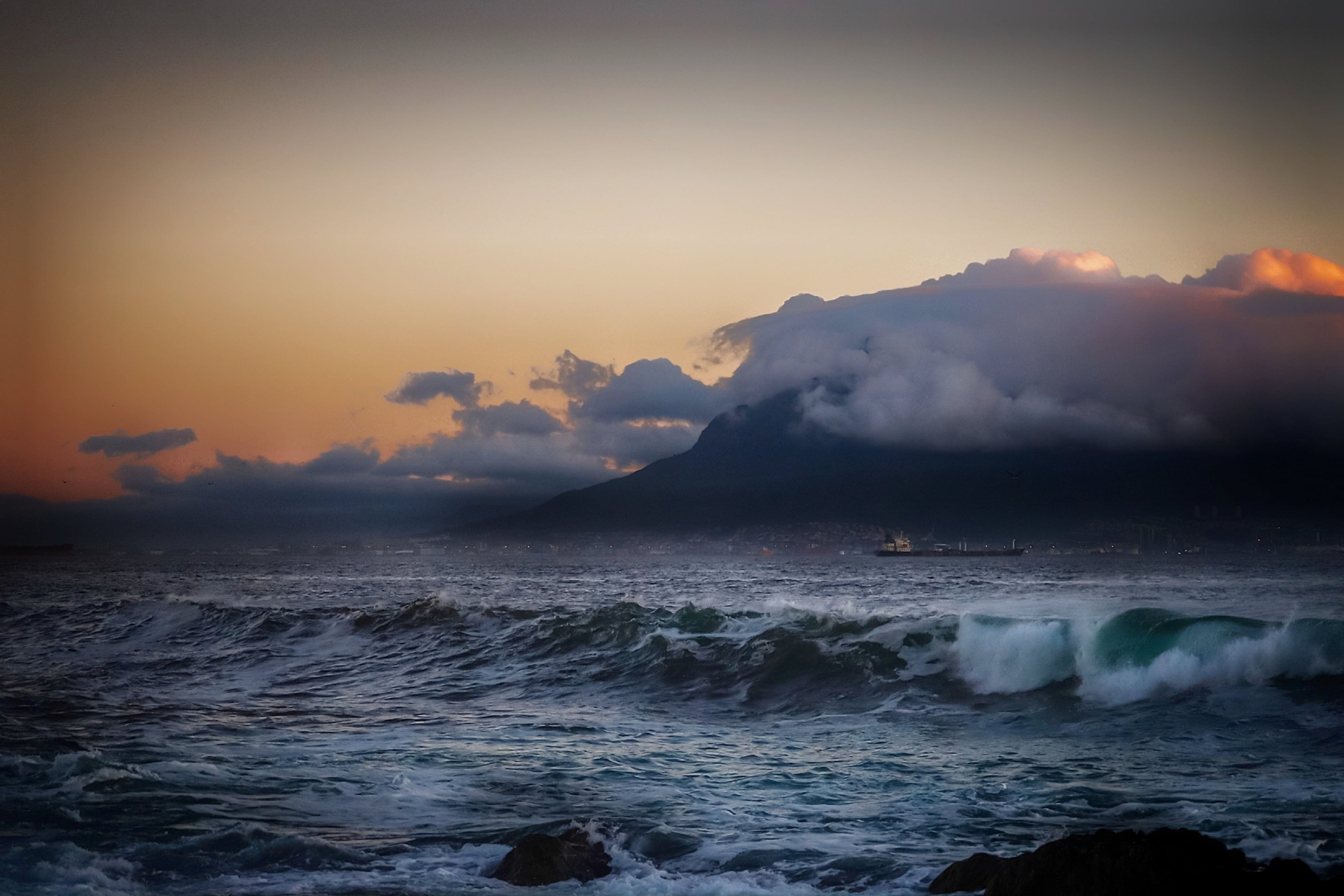 Fine art photograph of Table Mountain shrouded in storm cloud at dusk with dark Atlantic swells and amber sky over Table Bay, Cape Town South Africa seascape wall art print, ApertureAndArt.