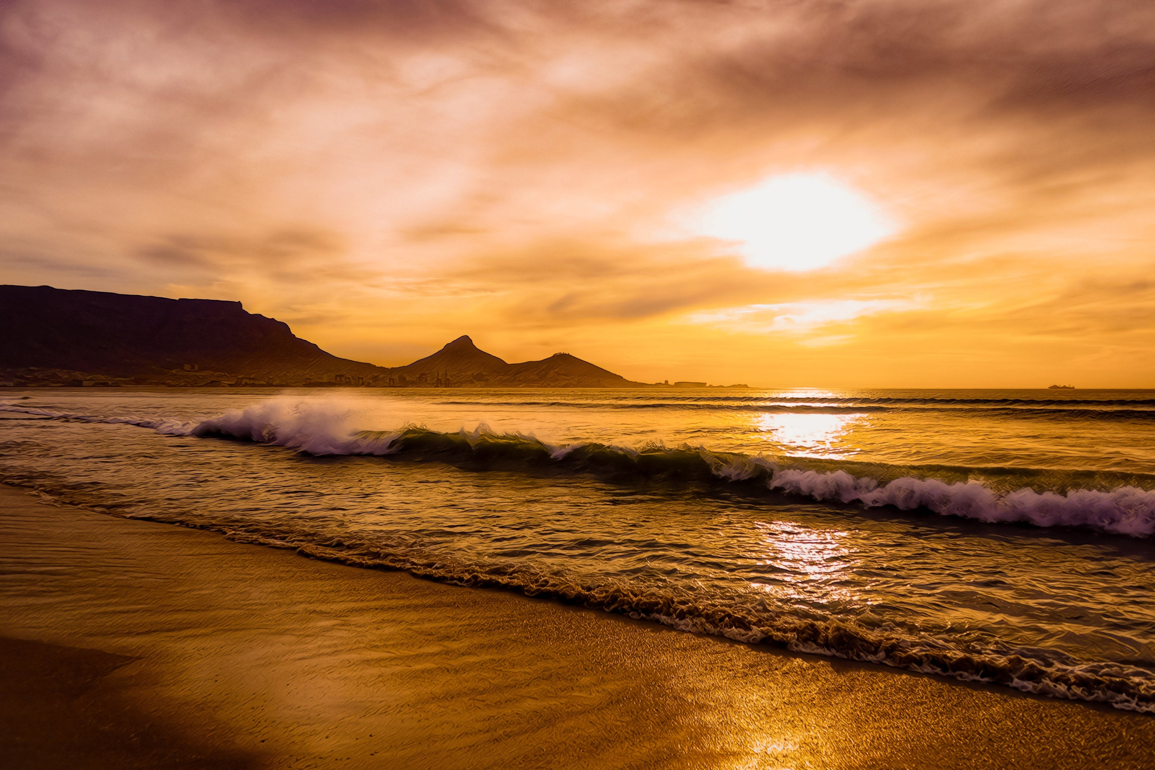Golden sunset over Table Mountain with rolling ocean waves and glowing reflections along the shoreline on South Africa’s west coast..