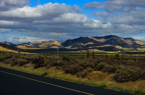 Scenic view of a mountain range with a road and power lines in the foreground.