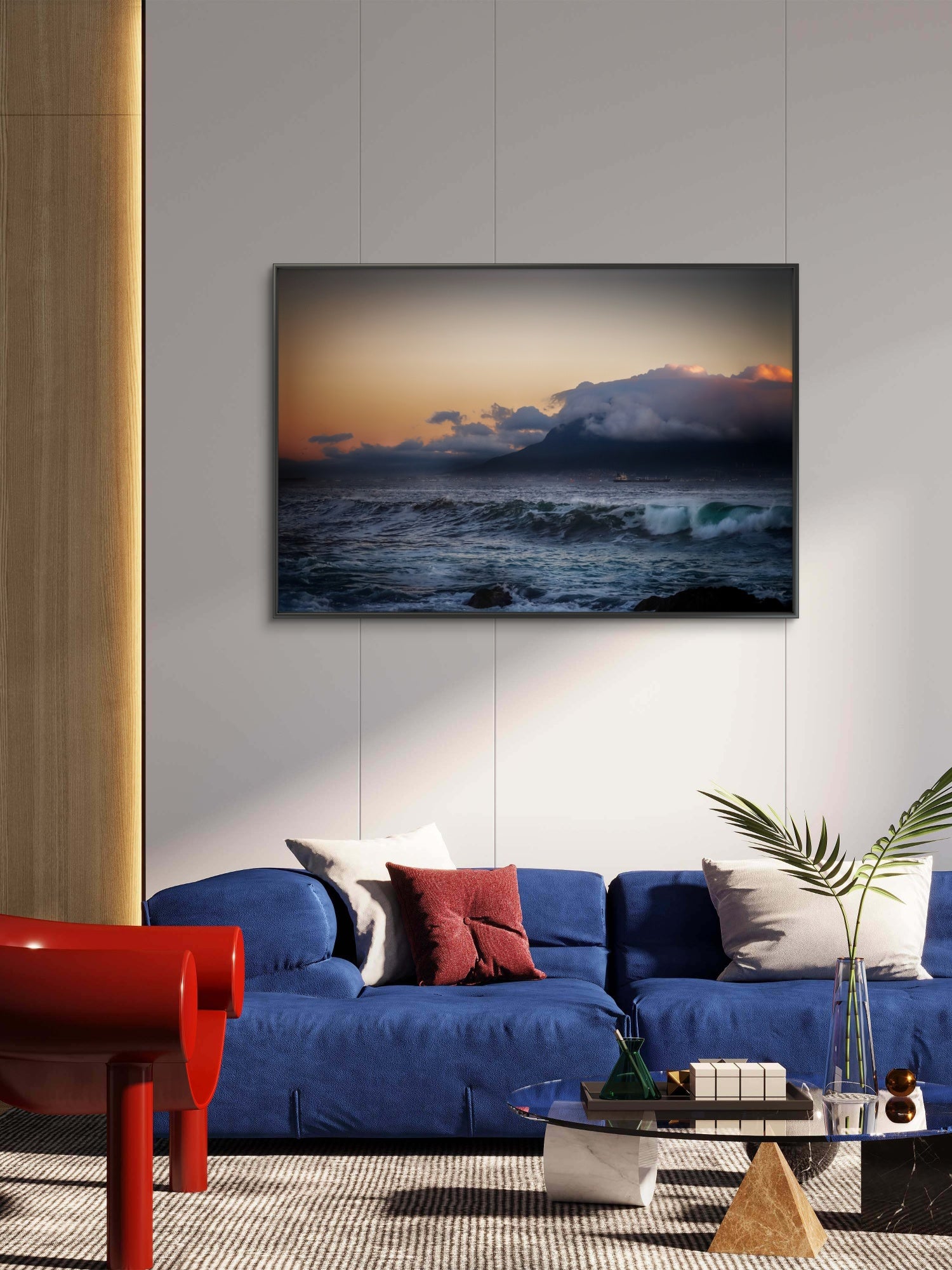 Modern living room with a blue sofa, red chair, and a large TV displaying a sunset over water.